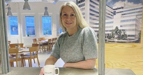 Marina Sjöström vid ett bord med ny vårbyggnad på bild bakom.