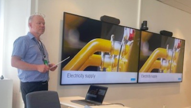 En man står framför två storbildsskärmar och håller en presentation.