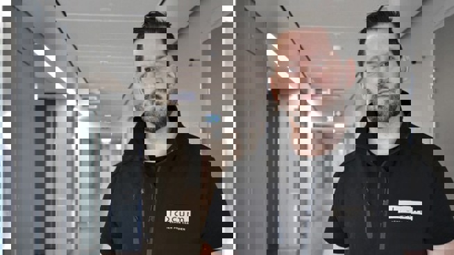 En man i svart Locumväst står i en sjukhuskorridor.