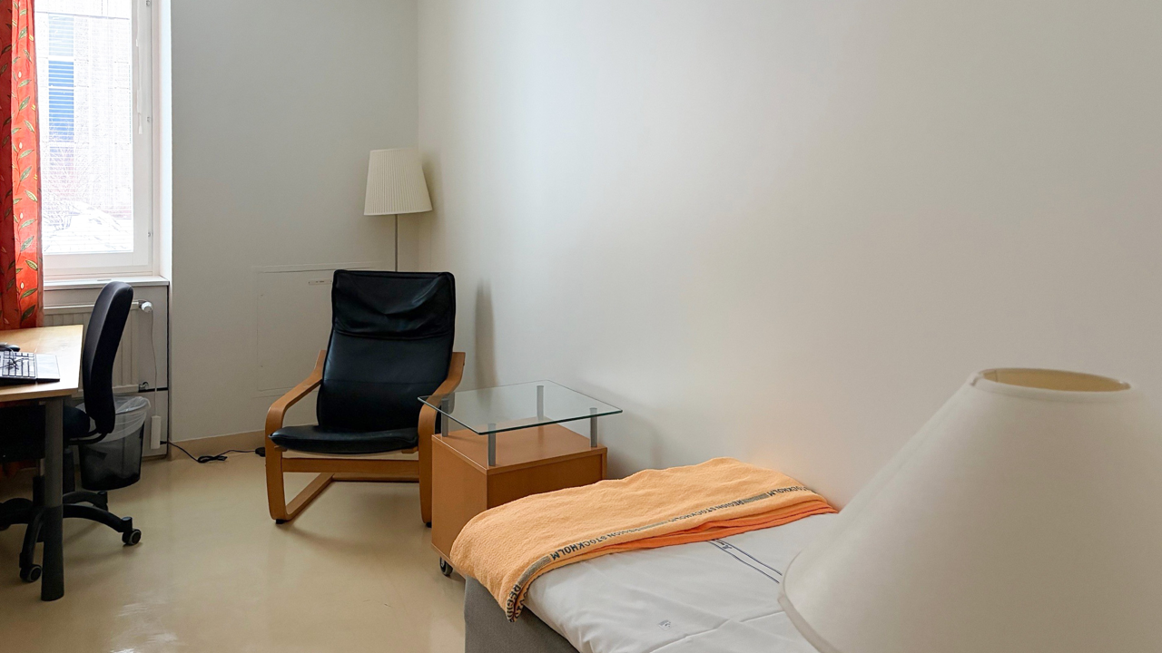 Ett rum med säng, skrivbord, stol och lampa.