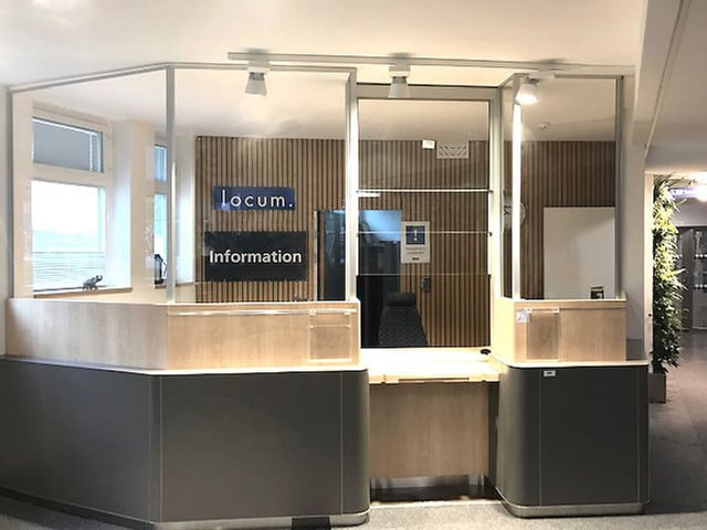 En receptionsdisk i grått och träfärgat. Glaslucka för service.