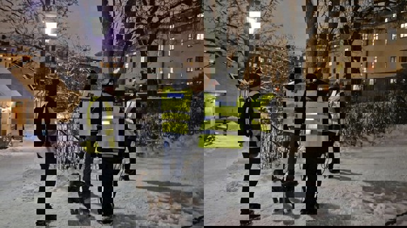 En grupp män som står bredvid en hund på en snötäckt gata med gula reflexväster. De går en trygghetsrondering på Landstingstomten.