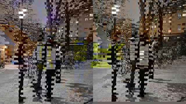 En grupp män som står bredvid en hund på en snötäckt gata med gula reflexväster. De går en trygghetsrondering på Landstingstomten.