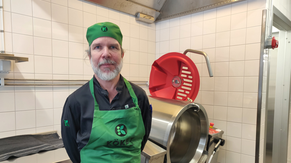 En kock står i ett kök bredvid en köksmaskin.