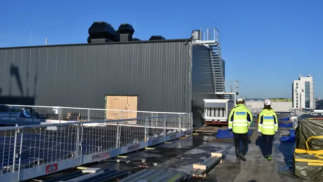 Två personer i varselkläder går på ett sjukhustak. 