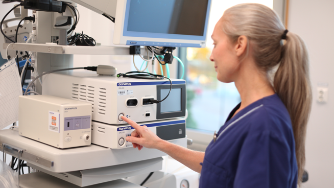 Kvinna i vårdkläder står vid medicinskteknisk utrustning och trycker på en knapp.