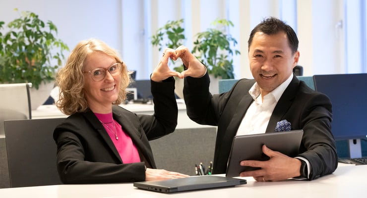 Två av Locums chefer står vid ett bord med en bärbar dator och gör hjärttecken med händer.