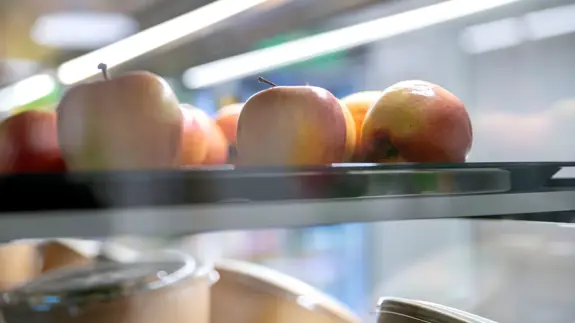 Äpplen och och sallader ligger på en hylla i en kyldisk. Delvis blurrig bild. 