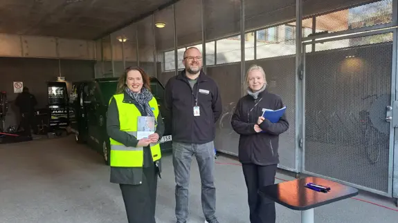 Tre personer som står bredvid varandra i ett garage.