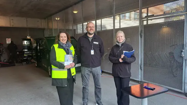 Tre personer som står bredvid varandra i ett garage.