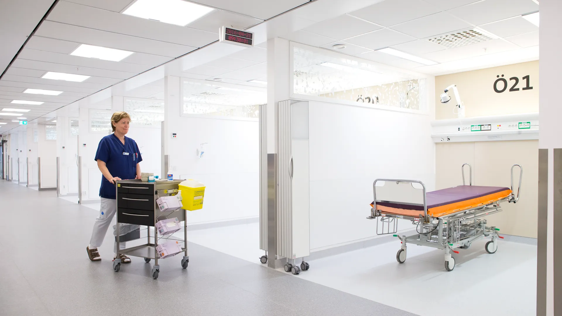 Ett akutb&aring;s med en sjuksk&ouml;terska som skjuter p&aring; en v&aring;rdvagn. I b&aring;set st&aring;r det en brits.