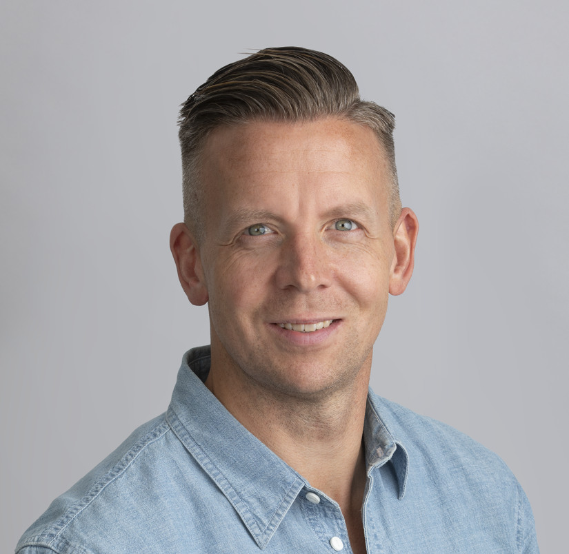 En man i en blå skjorta som ler mot kameran.