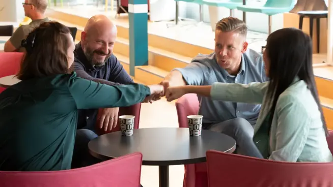 Fyra medarbetare runt ett bord med händer mot varandra.