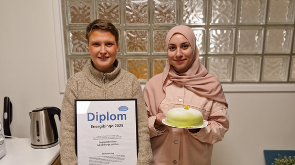 Två kvinnor, den ena står med ett diplom och den andra med en prinsesstårta.