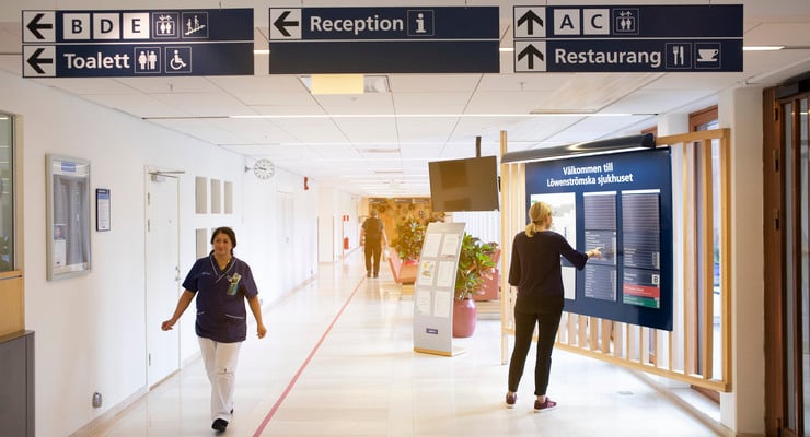 Kvinna st&aring;r och tittar p&aring; skyltar i sjukhuskorridor.