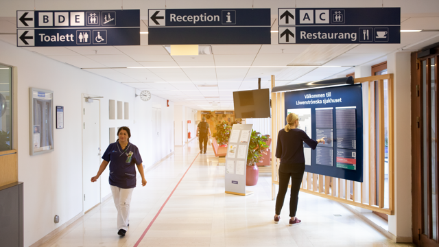Kvinna står och tittar på skyltar i sjukhuskorridor.