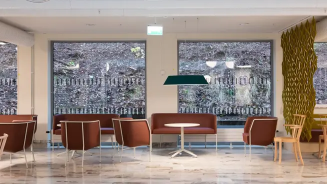 Stor vänthall i entrén med stora fönster, flera sittplatser och bord.