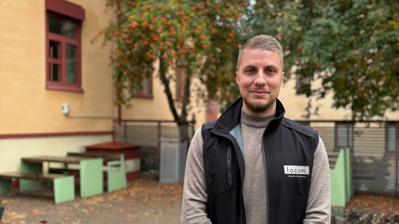 Man i svart väst står framför en byggnad och ler.