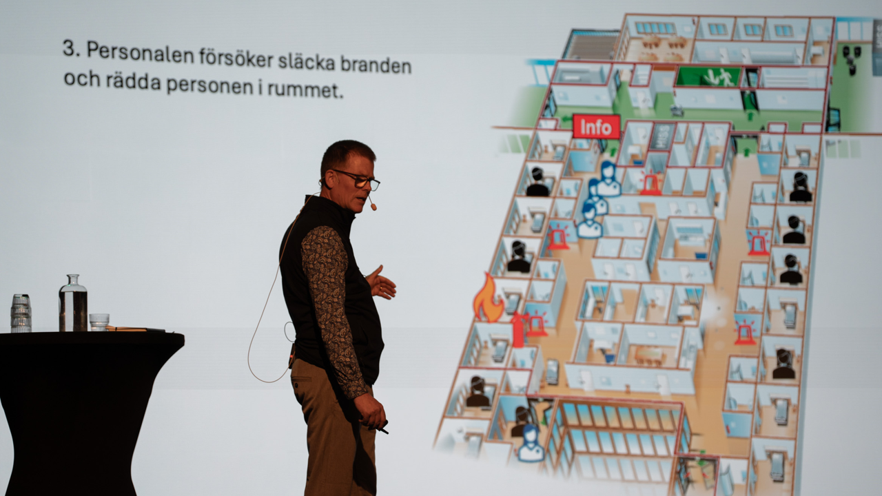 Man st&aring;r och f&ouml;rel&auml;ser p&aring; scen med publik.