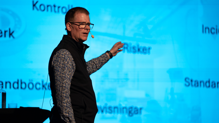 Man står och föreläser på scen med publik.