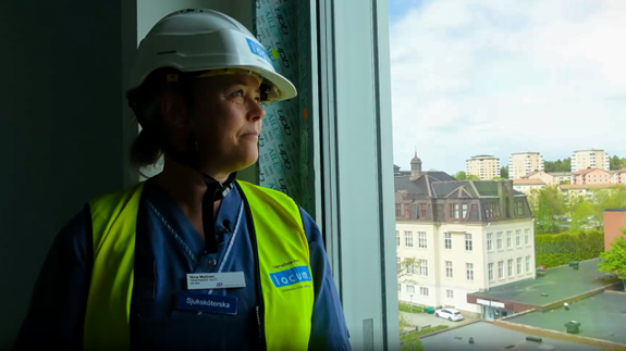 En person i bygghjälm står och tittar ut genom ett fönster. 