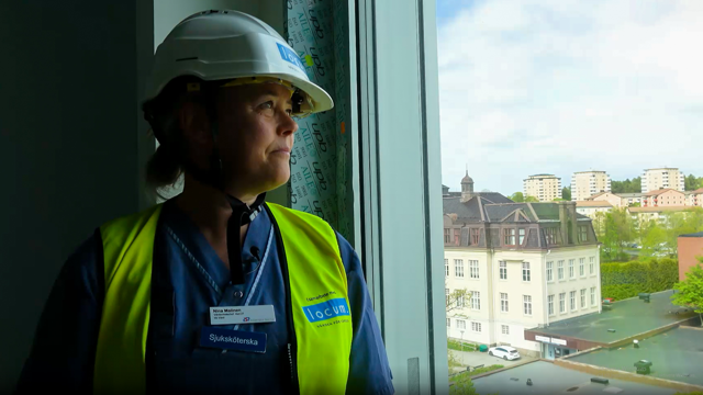 En person i bygghjälm står och tittar ut genom ett fönster. 