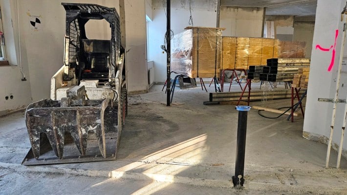 Ett rum i betong. I förgrunden står den en bobcat. I bakgrunden ser man rader med playwoodskivor.