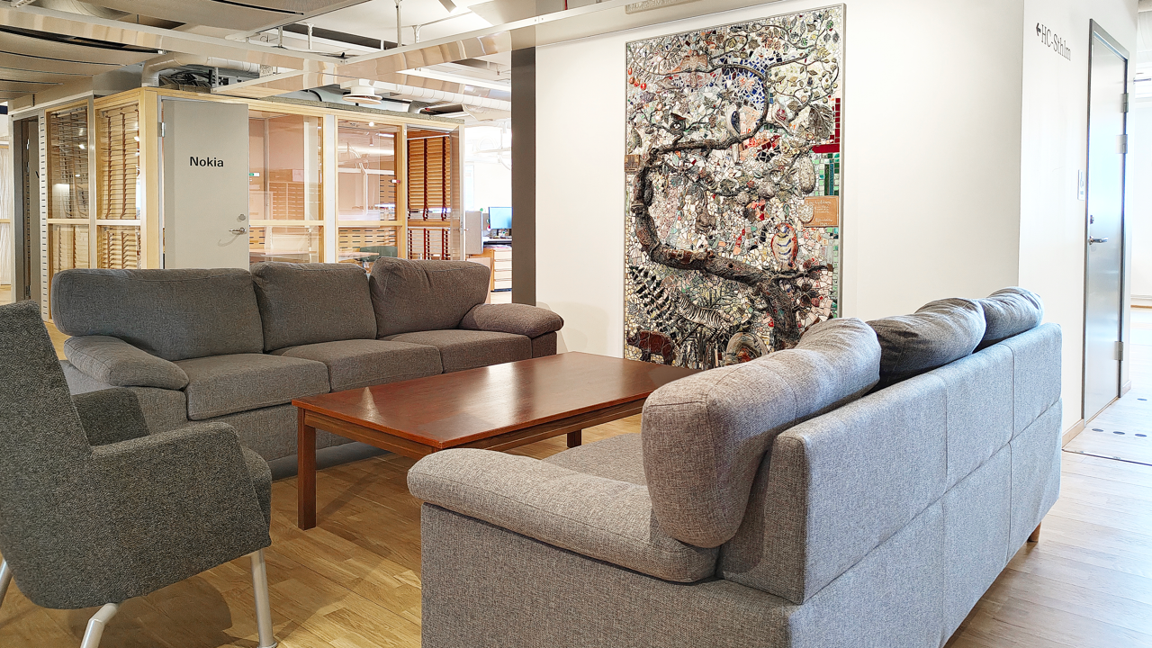 En soffgrupp i ett kontorslandskap med ett konstverk p&aring; v&auml;ggen.