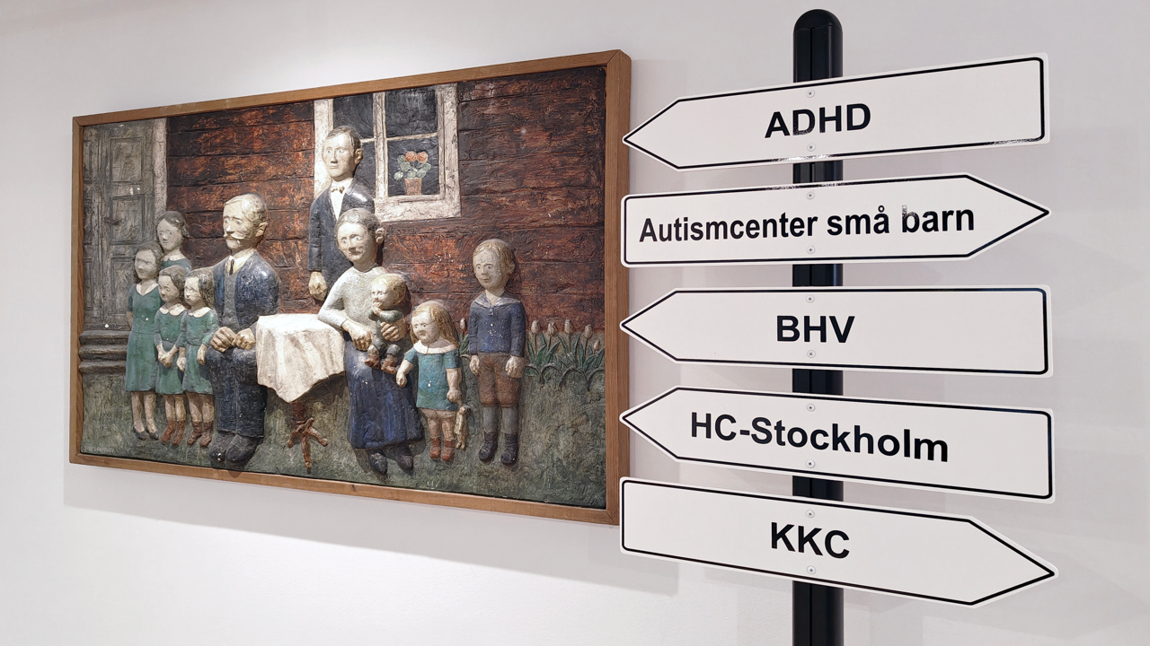 Ett konstverk p&aring; v&auml;ggen och stolpe med skyltar till olika verksamheter.