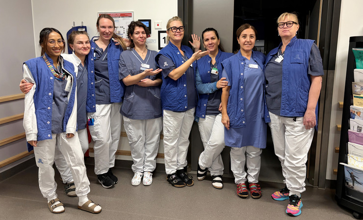 En grupp fr&aring;n Ortopedmottagningen vid Danderyds sjukhus framf&ouml;r ett nedsl&auml;ckt rum.