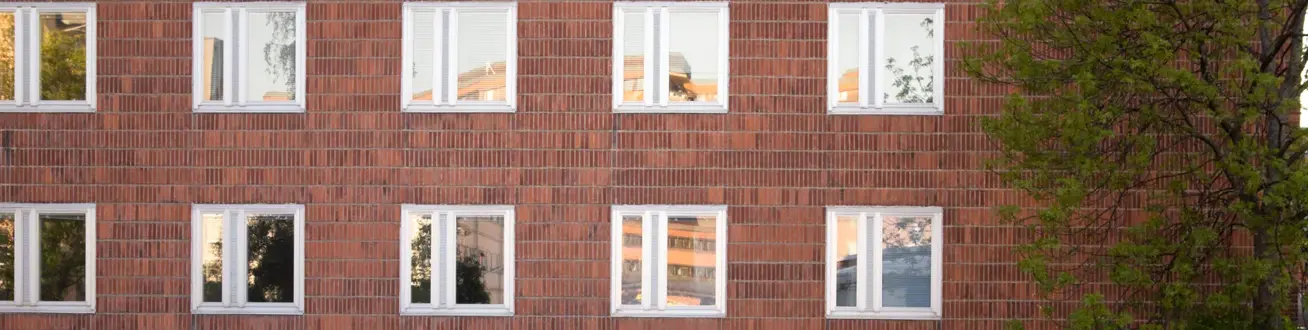 En röd tegelbyggnad med vita fönster. Ett träd på höger sida.