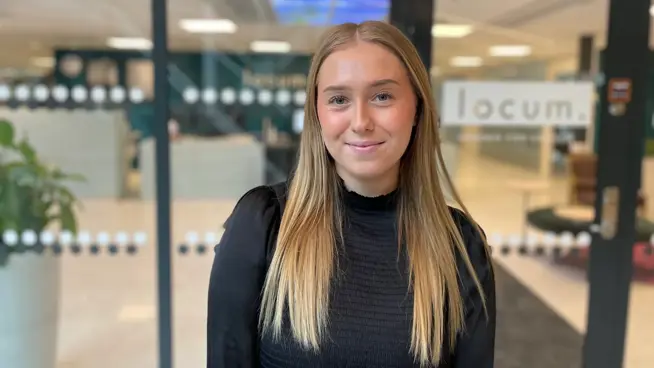 Ella står framför glasade entrédörrar med Locums logga. 
