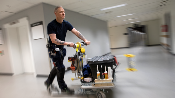 Driftpersonal åker sparkcykel i sjukhuskorridor.