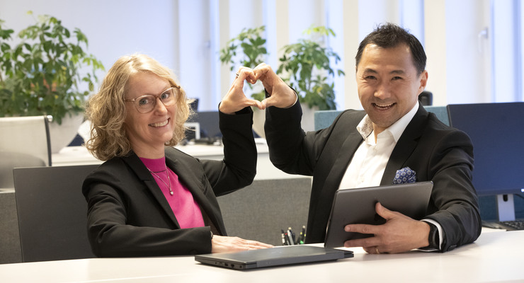 Två av Locums chefer står vid ett bord med en bärbar dator och gör hjärttecken med händer.