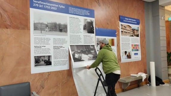 Planscher sätts upp på en stenvägg, man på stege arbetar.