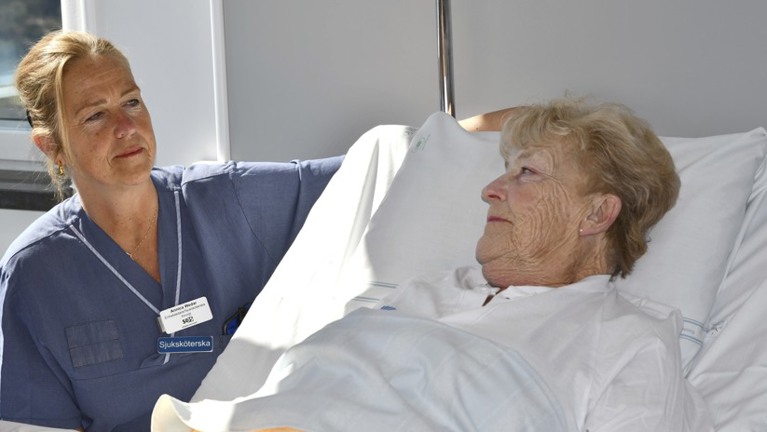 En kvinna som ligger i en sjukhussäng bredvid en sjuksköterska