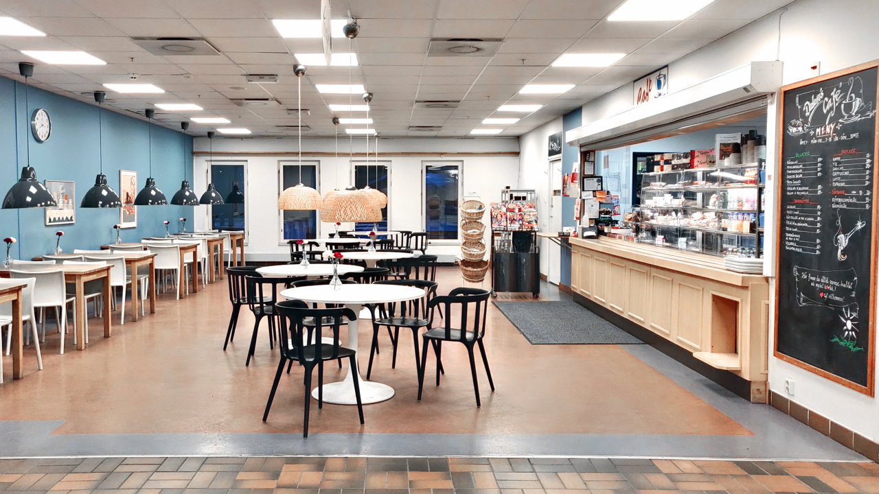 En cafeteria med bord och stolar och en griffeltavla.
