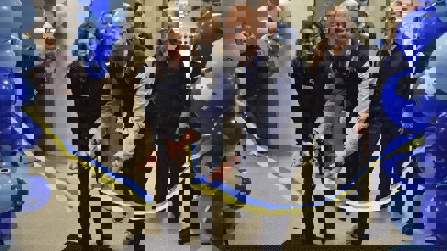 En kvinna och en man klipper ett blågult band, ballonger i blå nyanser och publik i bakgrunden.