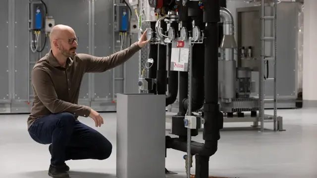 En man knäböjer bredvid en maskin.