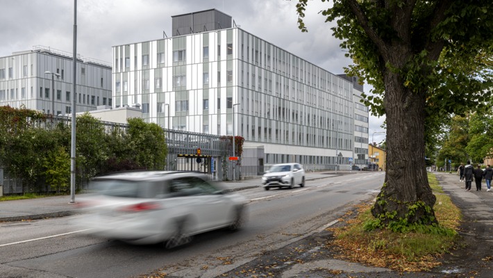 En vit bil som k&ouml;r l&auml;ngs en gata bredvid hus 20.