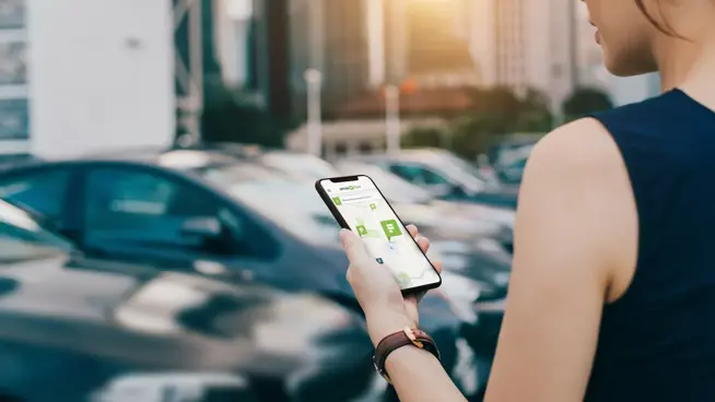 En kvinna som står på en parkeringsplats och tittar på sin mobiltelefon.