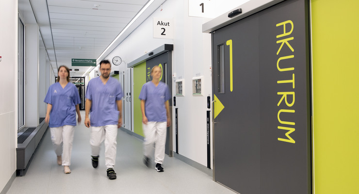 Tre personer i vårdkläder går i vårdkorridor.