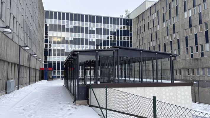 Ett cykelgarage mellan tv&aring; stora huskroppar.