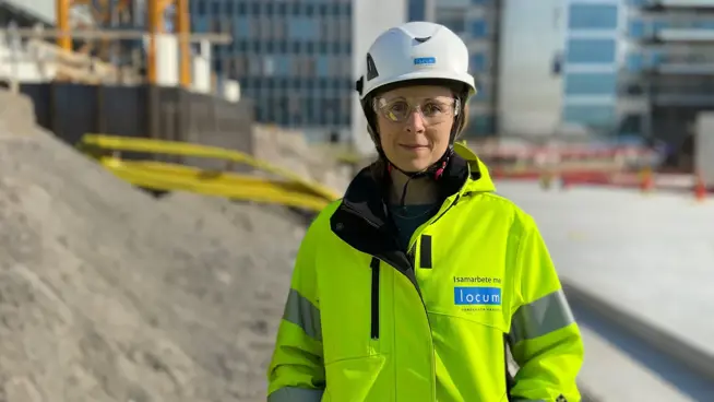 Sara står på byggarbetsplats med byggkläder.