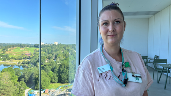 Kvinna i ljus t-shirt står på en balkong med utsikt över Edsviken.