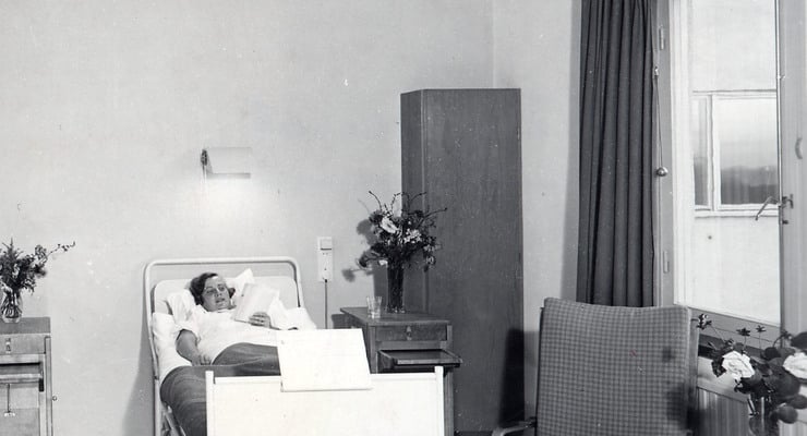 Äldre svartvitt foto av en patient i en vårdsäng med utsikt över Årstaviken.