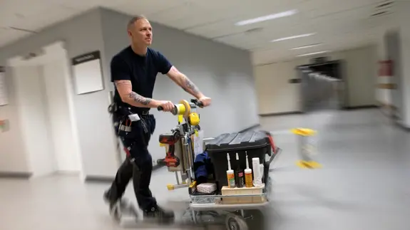 Driftpersonal åker sparkcykel i sjukhuskorridor.