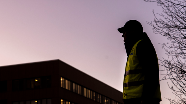 En locum personal
 som står framför en hög byggnad. Det är skymning.
