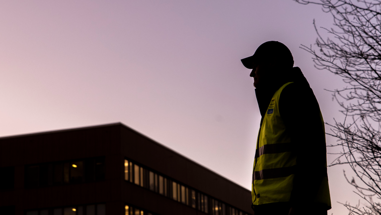 En locum personal
 som står framför en hög byggnad. Det är skymning.