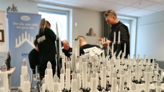 Flera ljusstakar står uppradade. Fyra personer i bakgrunden.